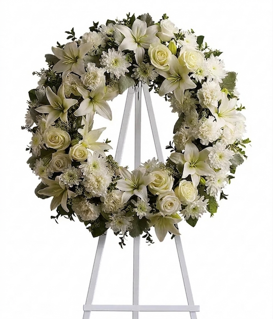 White sympathy wreath with lilies, roses, chrysanthemums, carnations, and greenery on an easel stand.